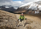 Sally braces against a 40 mph tail wind just above Siyeh Pass at 8100-ft.  A small avalanche pours off Mt. Siyeh abover and to the right...