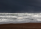 Dark clouds distant; chaotic waves lit by the morning sun.  LIncoln Beach, OR